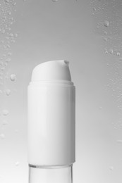 Photo of Bottle with moisturizing cream on grey background, view through wet glass