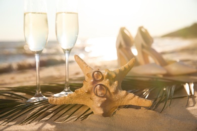 Photo of Starfish with gold wedding rings and glasses of champagne on sandy beach