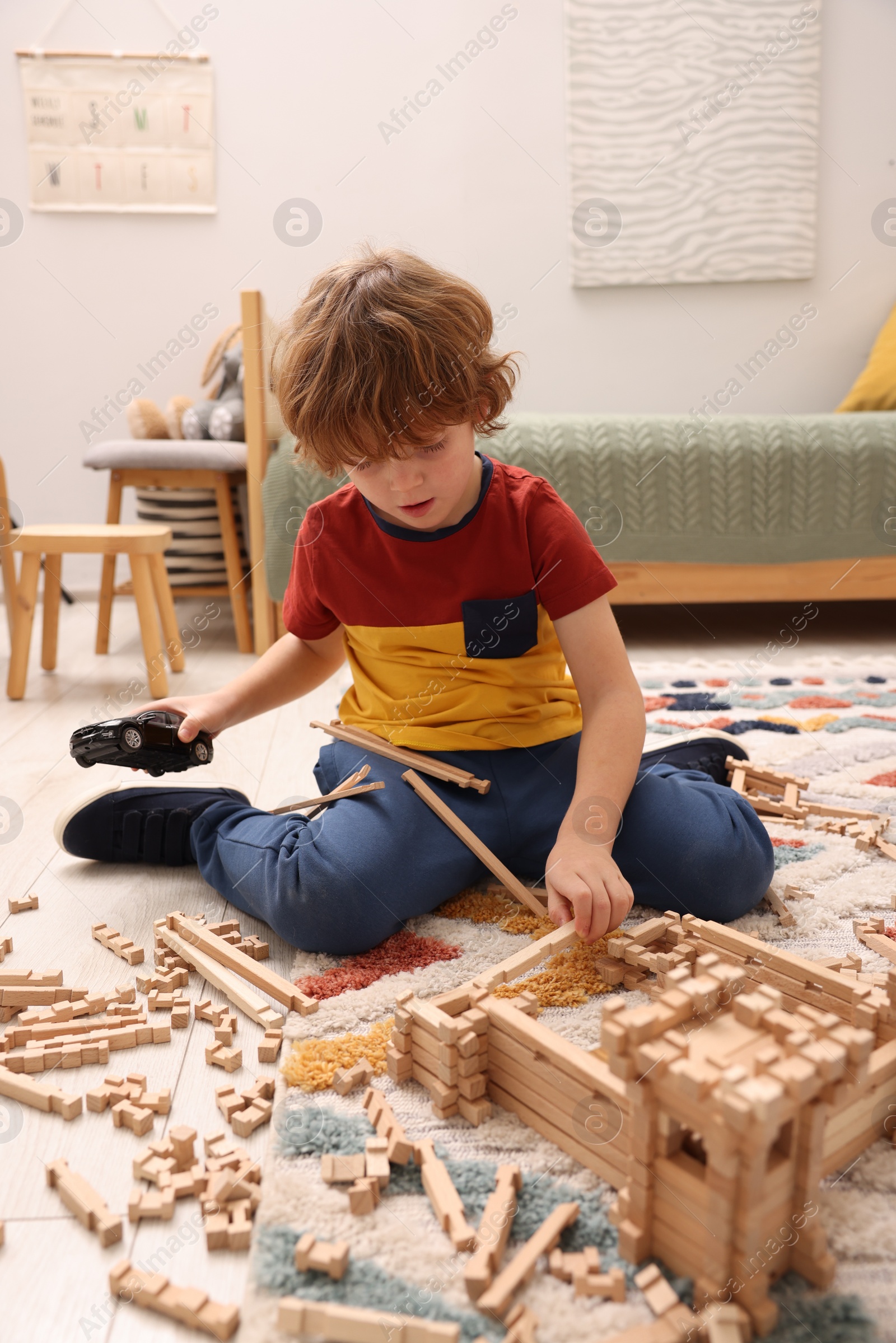 Photo of Little boy playing with wooden construction set on carpet in room. Child's toy