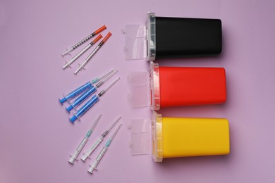 Photo of Disposable syringes with needles and sharps containers on violet background, flat lay