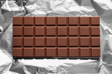 Photo of Delicious milk chocolate bar on foil, top view