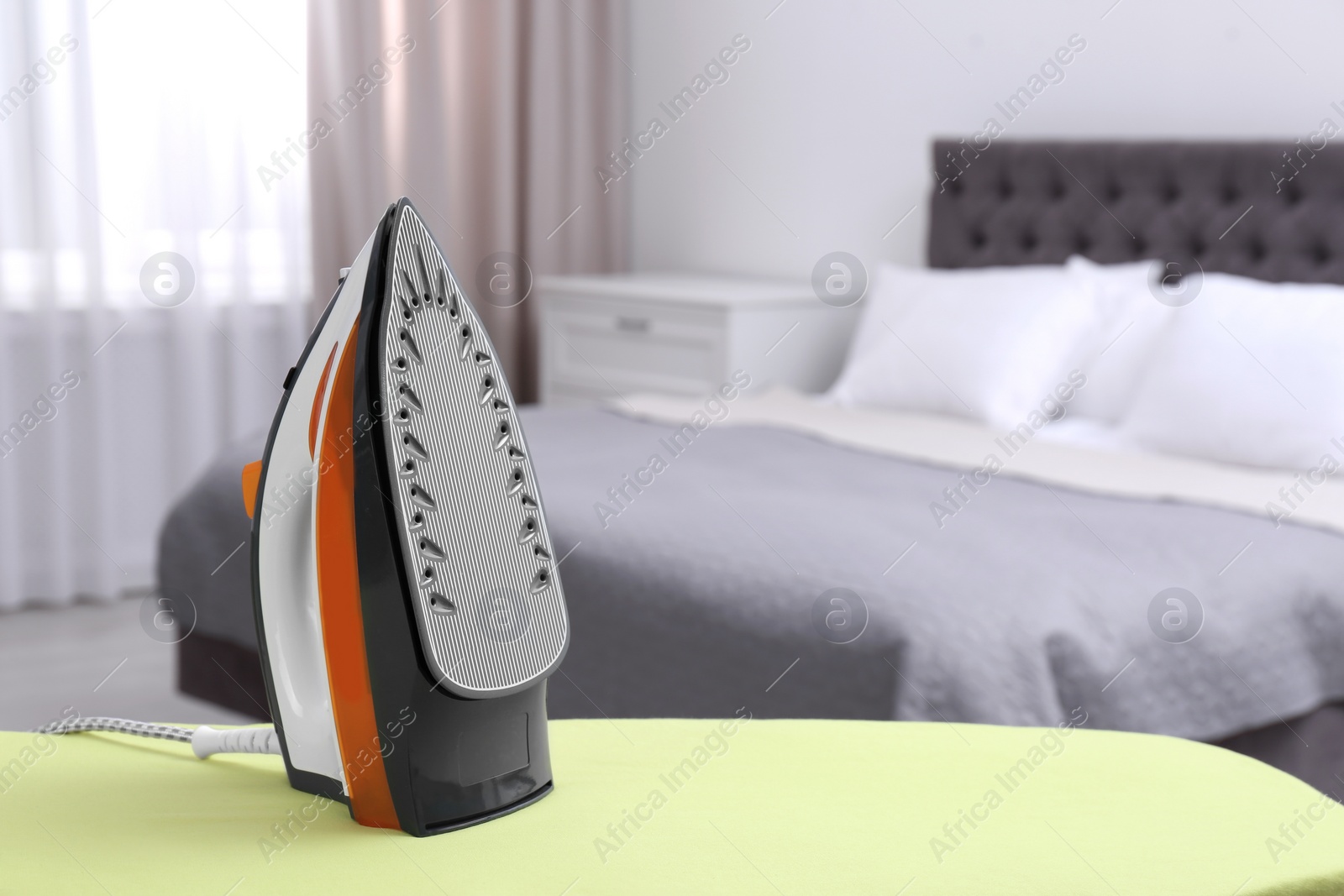 Photo of Modern electric iron on board in bedroom, space for text. Laundry day