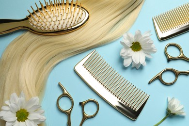 Flat lay composition with professional hairdresser tools, flowers and blonde hair strand on light blue background