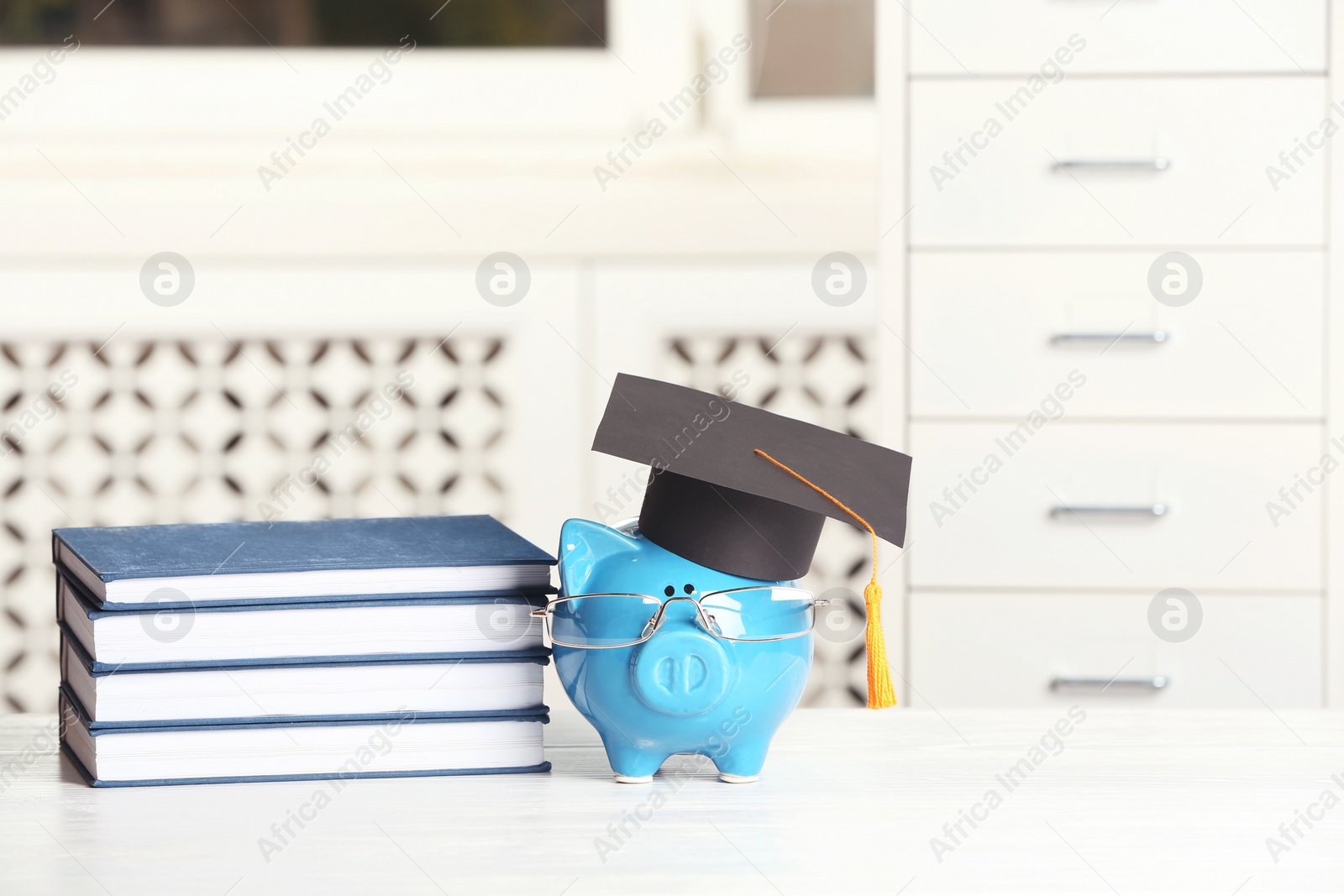 Photo of Piggy bank with graduation hat and books on table against blurred background