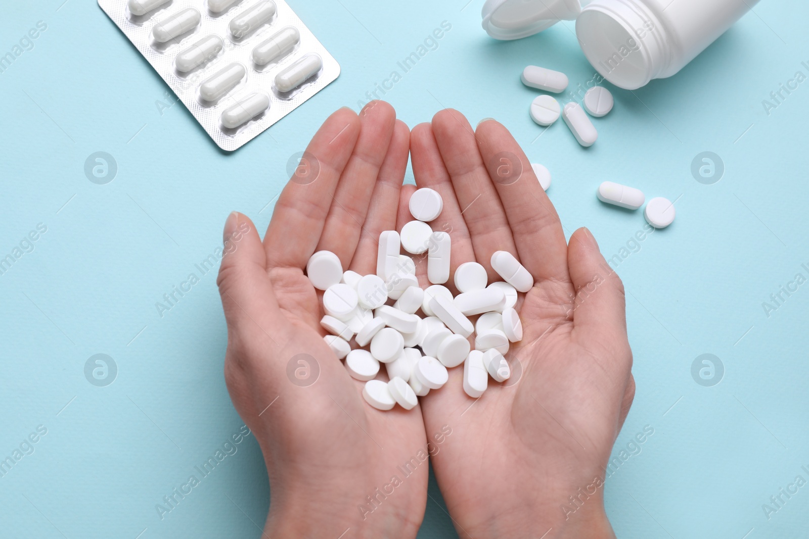 Photo of Woman holding antidepressants on light blue background, top view