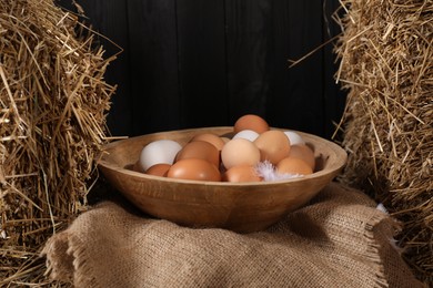 Photo of Fresh chicken eggs in bowl among dried straw bales