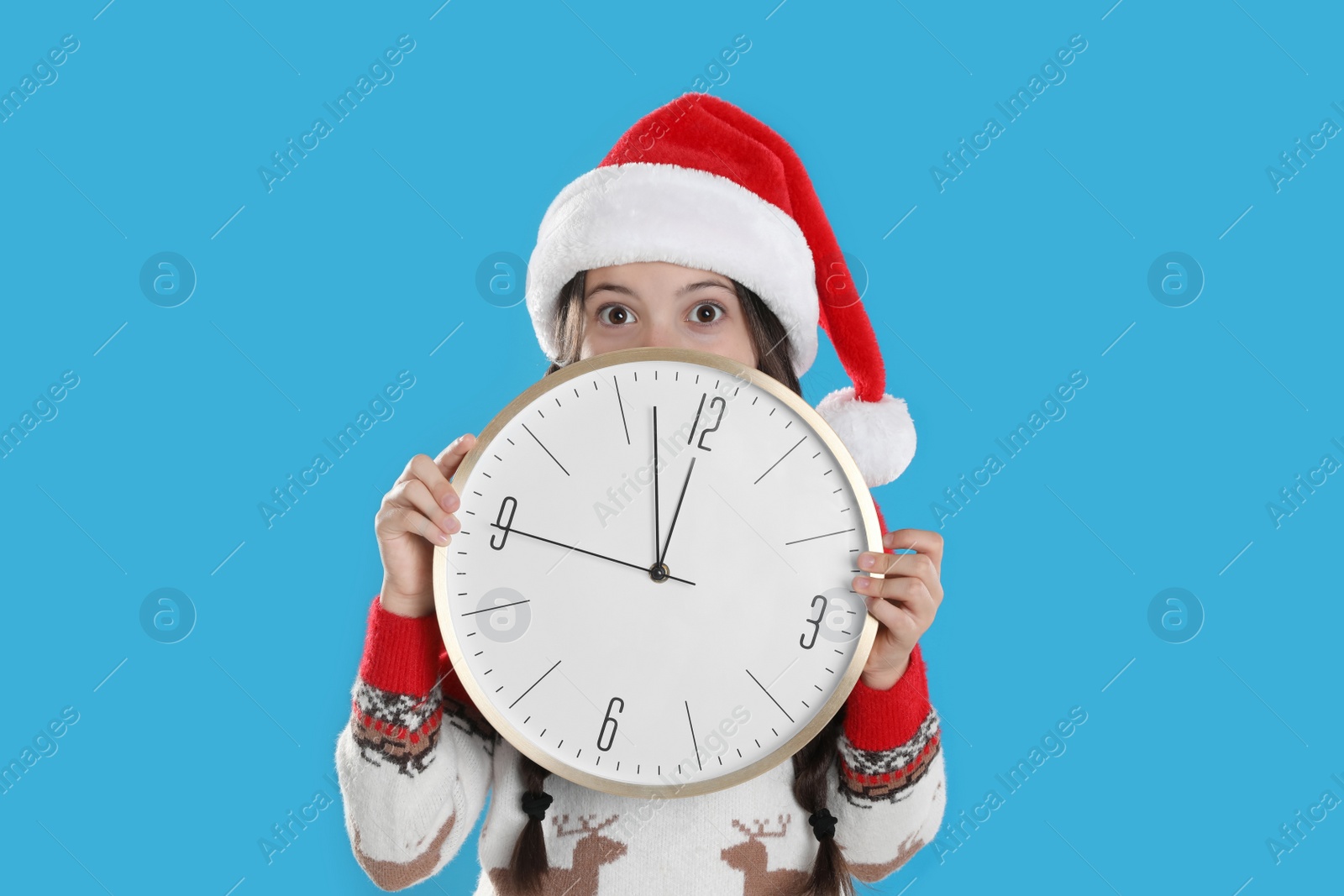 Photo of Girl in Santa hat with clock on light blue background. New Year countdown