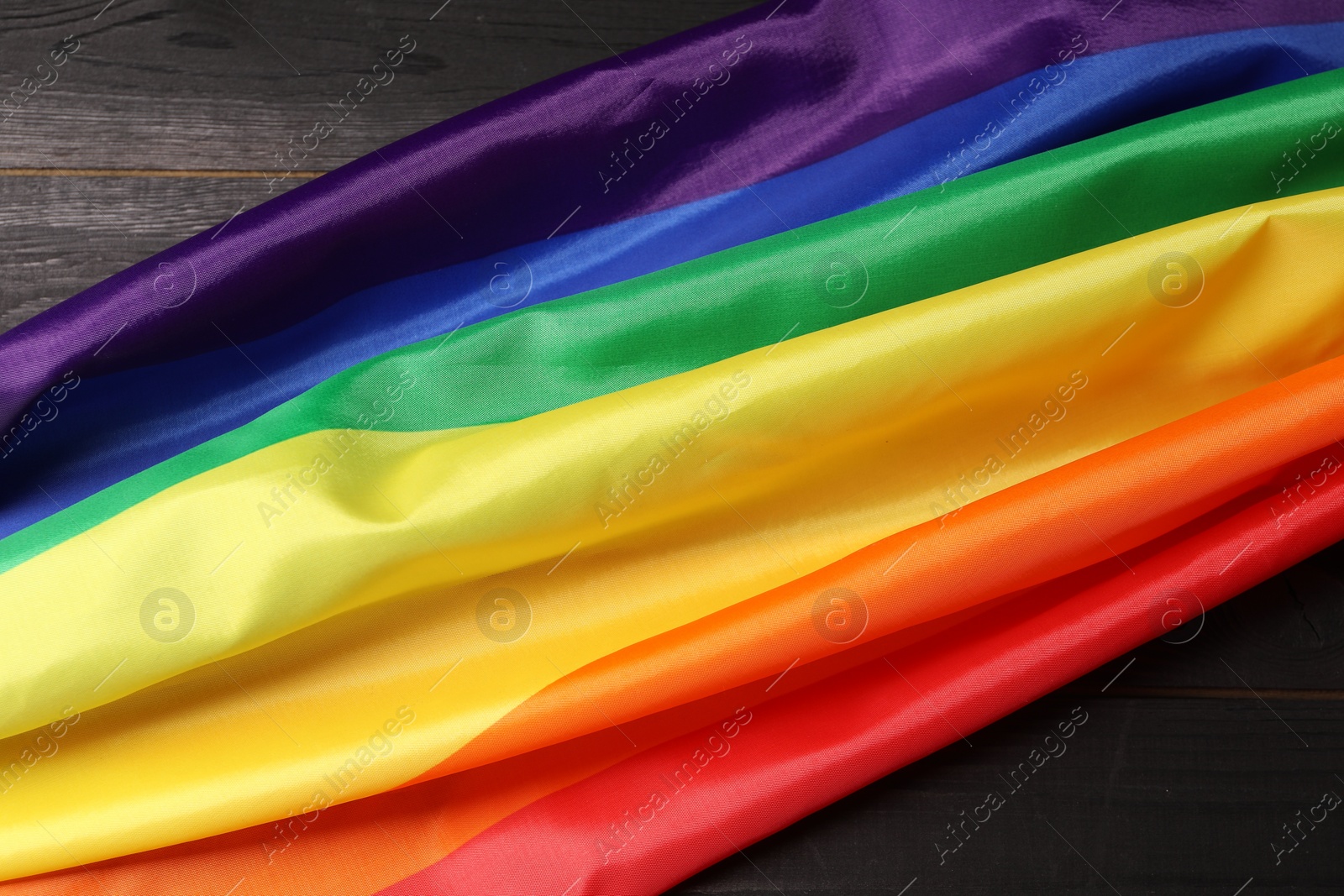 Photo of Rainbow LGBT flag on black wooden background, top view