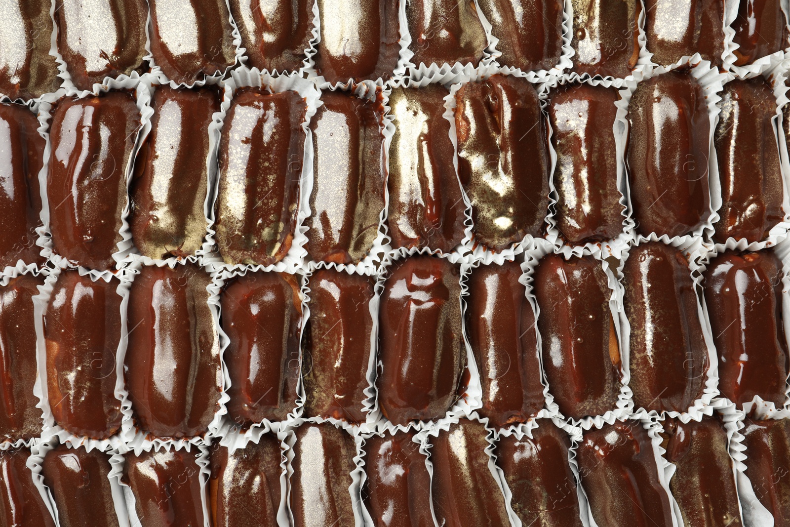 Photo of Many delicious eclairs with chocolate icing as background, top view