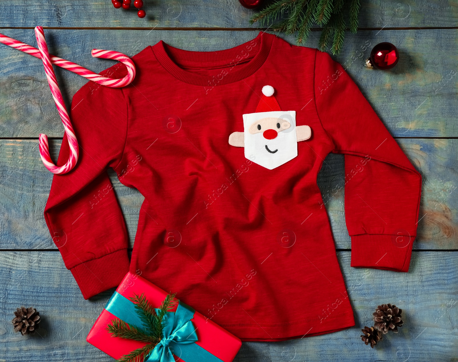 Photo of Red baby jumper and Christmas decorations on blue wooden background, flat lay