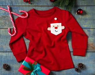 Photo of Red baby jumper and Christmas decorations on blue wooden background, flat lay