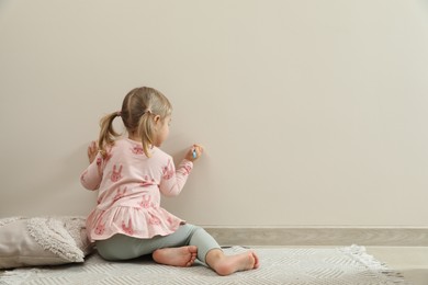 Photo of Little girl drawing on beige wall indoors, back view and space for text. Child`s art