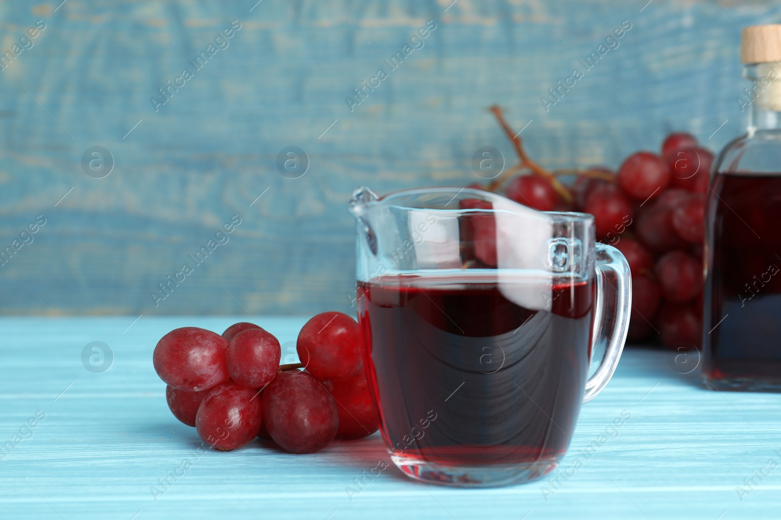 Photo of Glass jug with wine vinegar and fresh grapes on wooden table