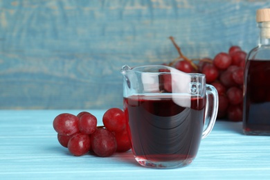 Photo of Glass jug with wine vinegar and fresh grapes on wooden table