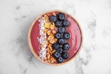 Bowl of delicious fruit smoothie with fresh blueberries, granola and coconut flakes on white marble table, top view