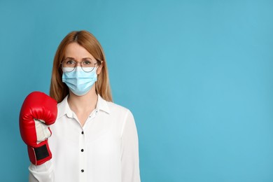 Photo of Woman with protective mask and boxing gloves on light blue background, space for text. Strong immunity concept