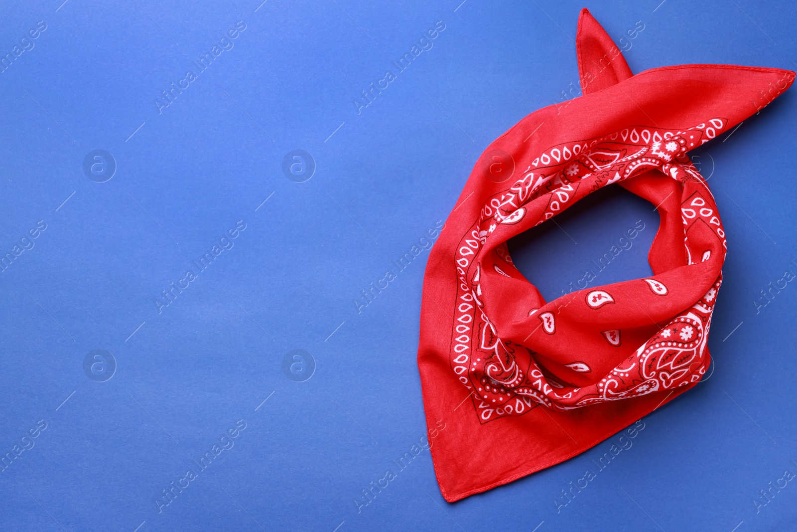 Photo of Folded red bandana with paisley pattern on blue background, top view. Space for text