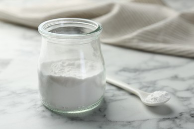 Photo of Baking powder in jar and spoon on white marble table, closeup. Space for text