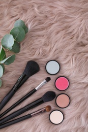 Flat lay composition with makeup brushes and cosmetic products on faux fur