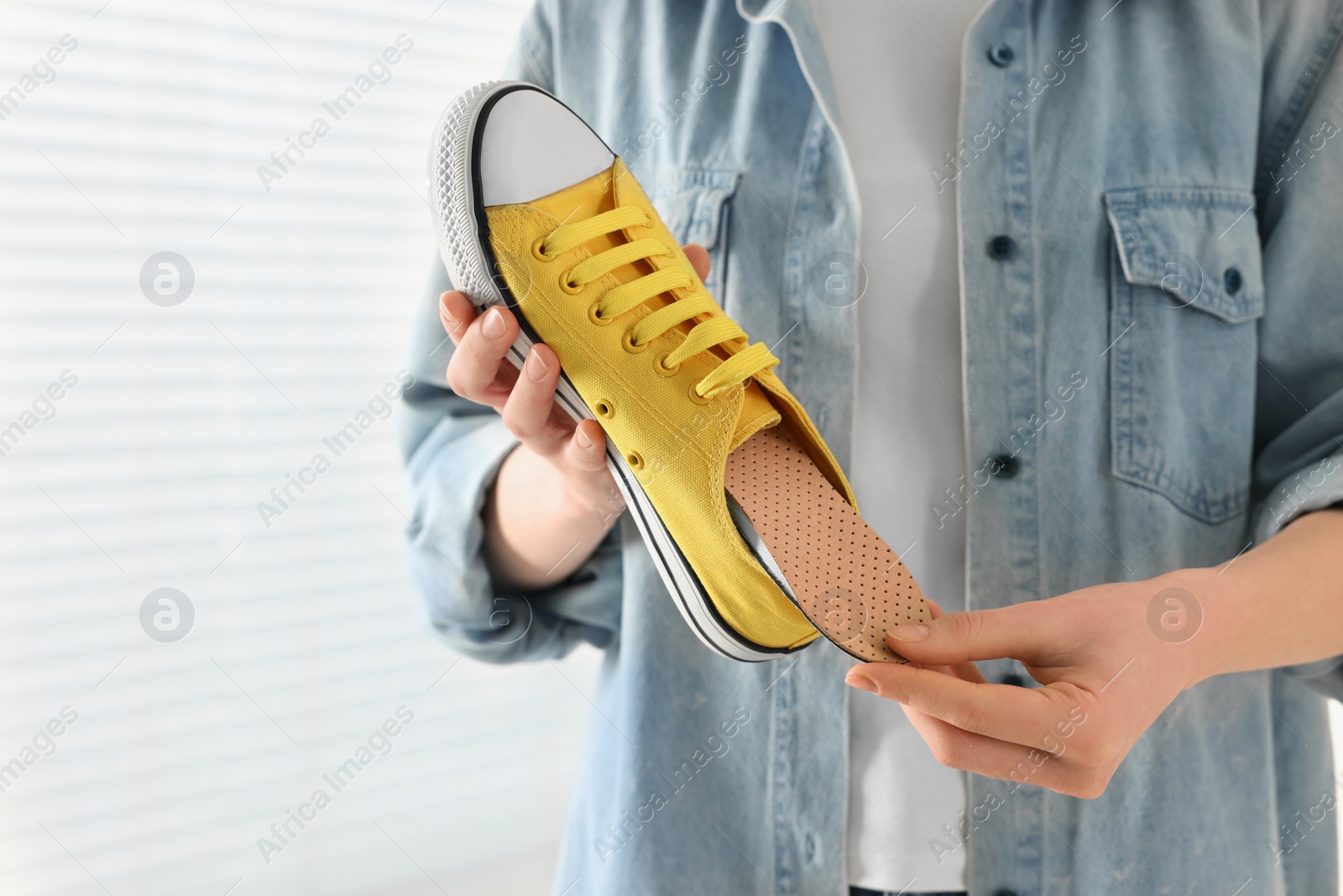 Photo of Woman putting orthopedic insole into shoe indoors, closeup. Foot care