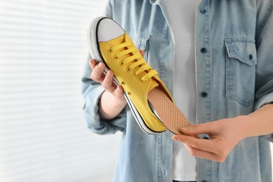Woman putting orthopedic insole into shoe indoors, closeup. Foot care