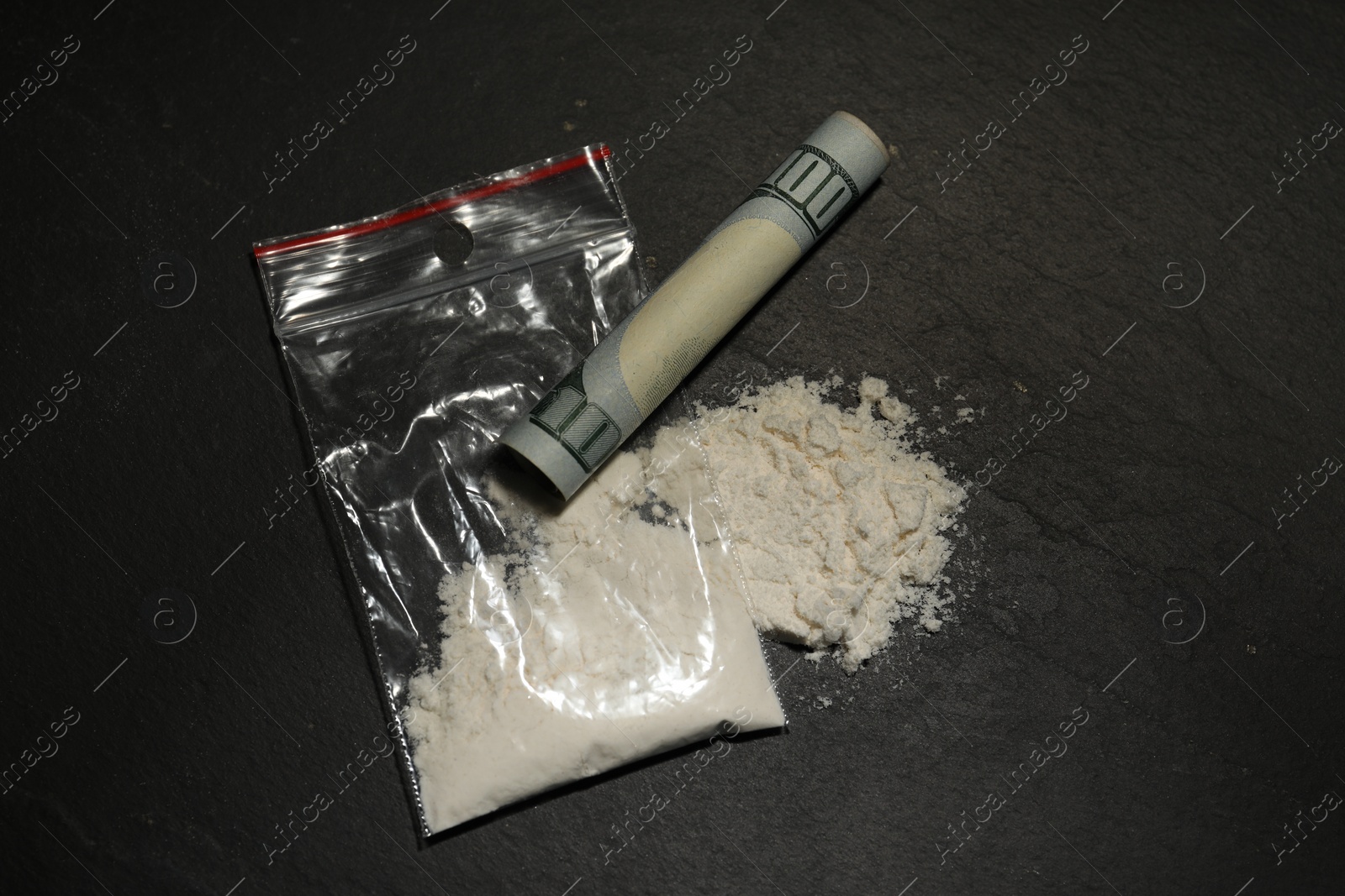 Photo of Drug addiction. Plastic bag with cocaine and rolled dollar banknote on grey textured background,, flat lay