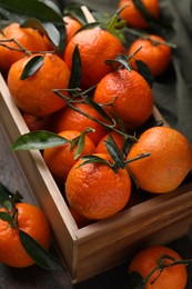 Photo of Fresh ripe tangerines with green leaves in crate on wooden table, above view