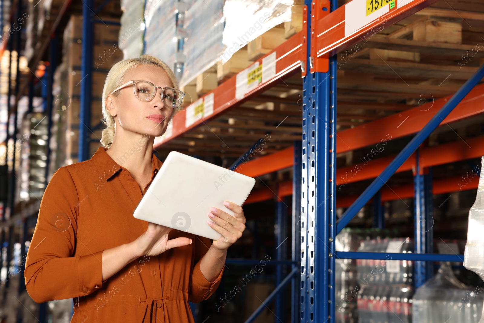 Photo of Happy manager using modern tablet in warehouse with lots of products