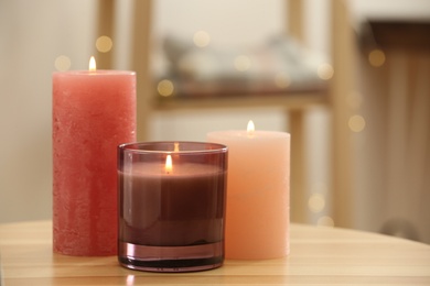 Stylish burning candles on wooden table indoors