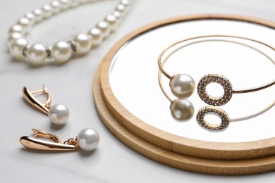 Photo of Elegant necklace, bracelet and earrings with pearls on white marble table, closeup