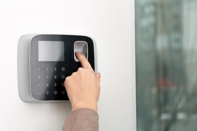 Woman scanning fingerprint on alarm system indoors, closeup. Space for text