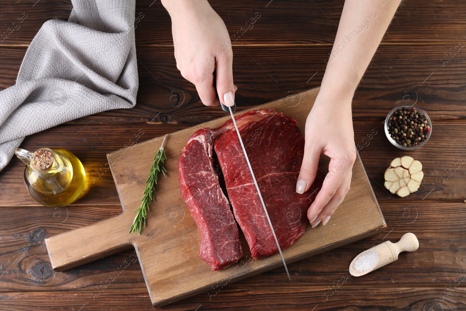 Photo of Woman cutting fresh raw beef steak at wooden table, top view