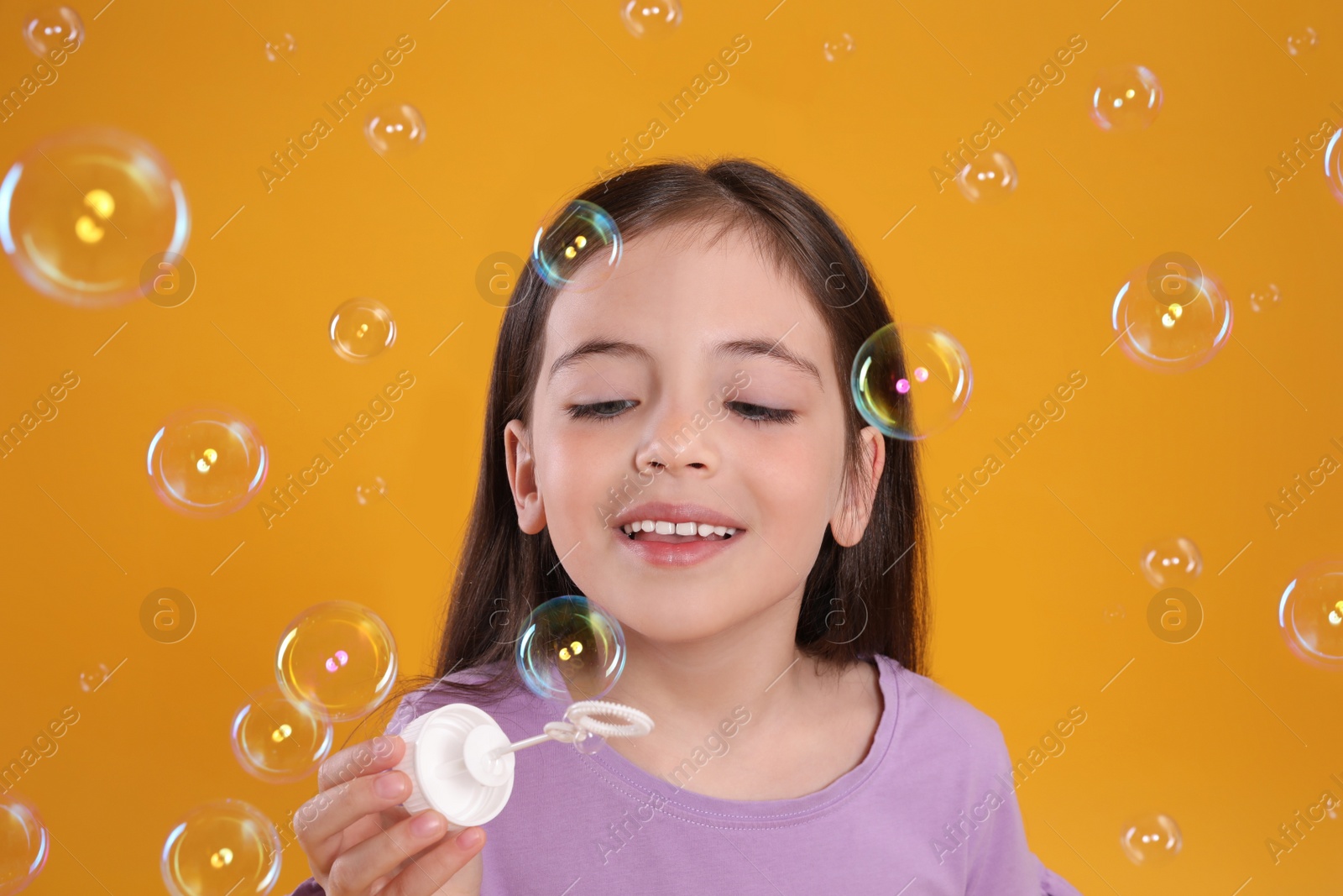 Photo of Little girl having fun with soap bubbles on yellow background