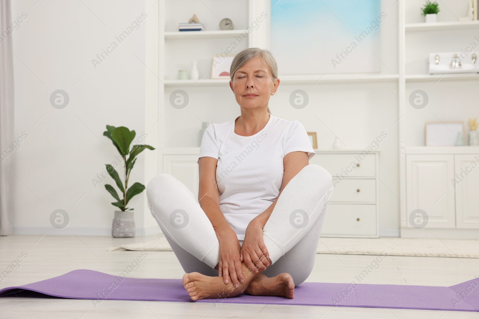 Photo of Senior woman practicing yoga on mat at home