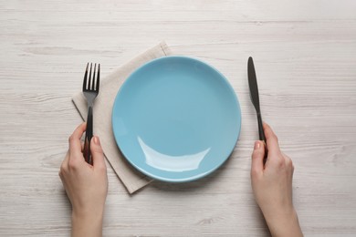Woman with empty plate and cutlery at white wooden table, top view
