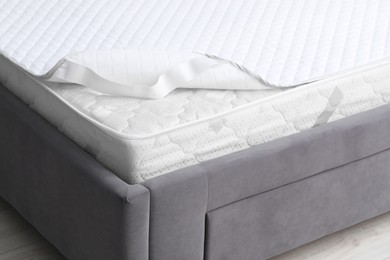 Photo of New soft mattress with protector on grey bed indoors, closeup