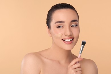 Photo of Woman with swatch of foundation holding makeup brush on beige background