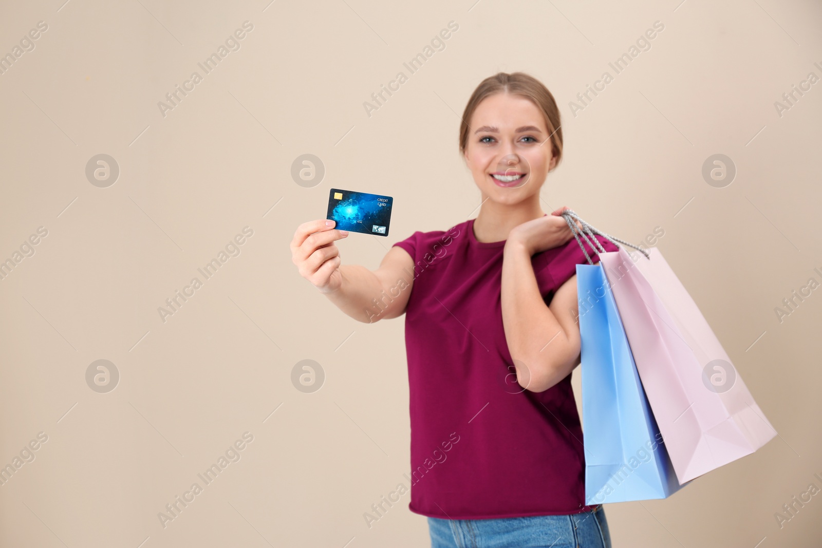 Photo of Portrait of happy young woman with credit card and shopping bags on color background, space for text. Spending money