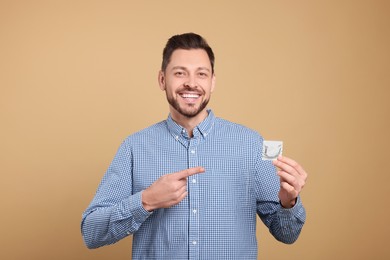 Photo of Happy man holding condom on beige background, closeup