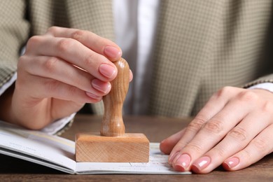 Photo of Ukraine, Lviv - September 6, 2022: Woman stamping visa page in passport at wooden table, closeup