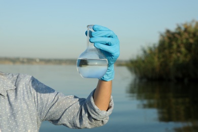 Photo of Scientist with florence flask taking sample from river for analysis, closeup