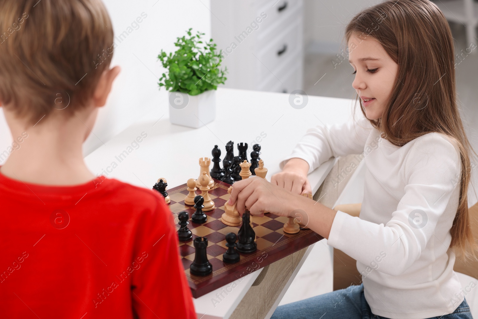 Photo of Cute children playing chess at table in room