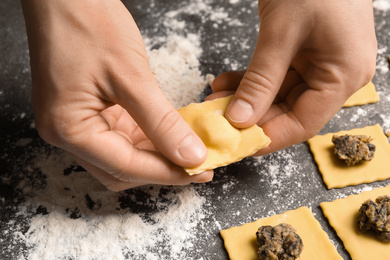 Woman making ravioli at grey table, closeup. Italian pasta