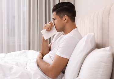 Sick man with tissue suffering from cold in bed at home