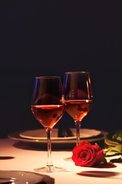 Photo of Beautiful table setting with glasses of wine and rose in dark room. Romantic dinner for Valentine's day