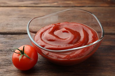 Photo of Bowl of tasty ketchup and tomato on wooden table, closeup