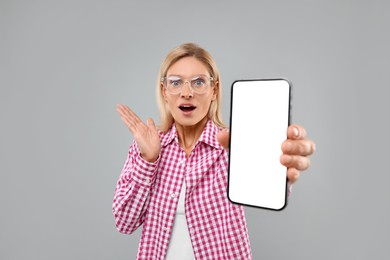 Surprised woman holding smartphone with blank screen in hand on grey background