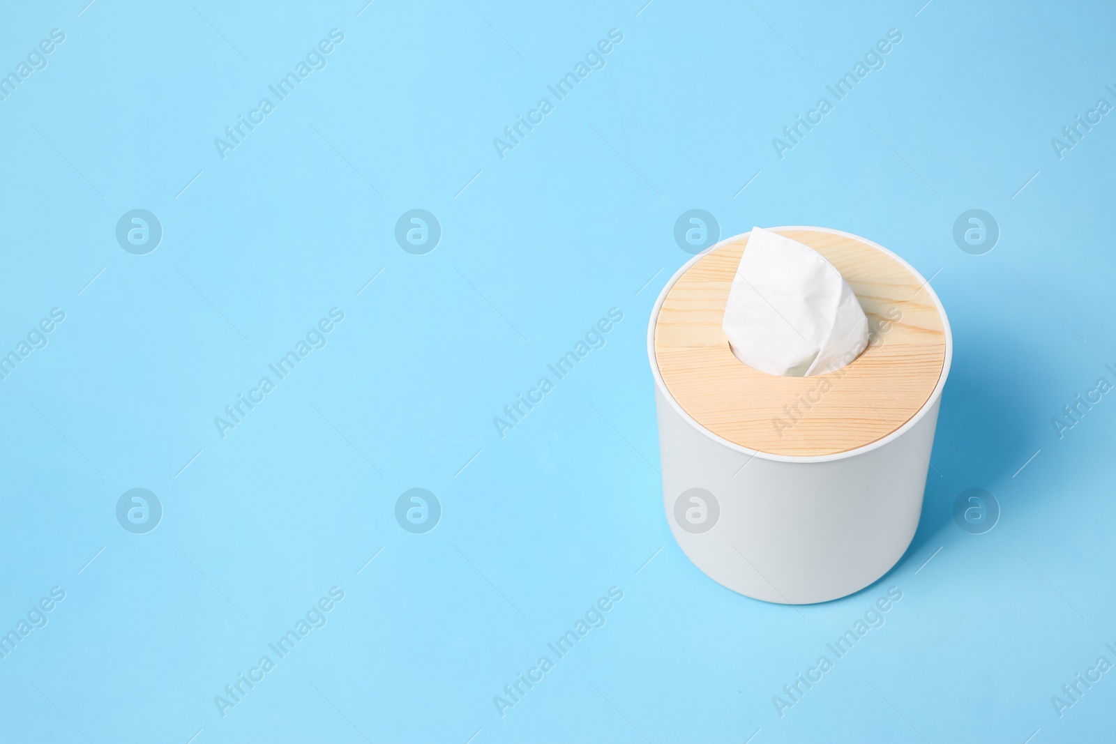 Photo of Holder with paper tissues on light blue background. Space for text