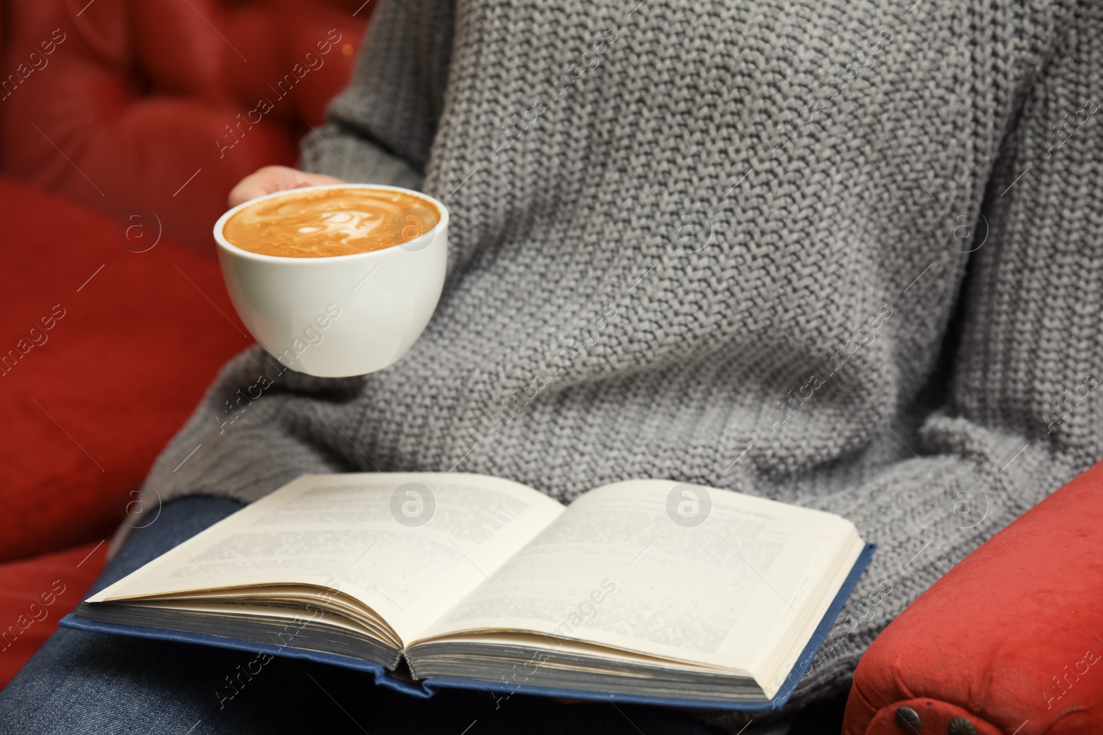 Photo of Woman with cup of coffee reading book on sofa, closeup