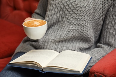 Photo of Woman with cup of coffee reading book on sofa, closeup
